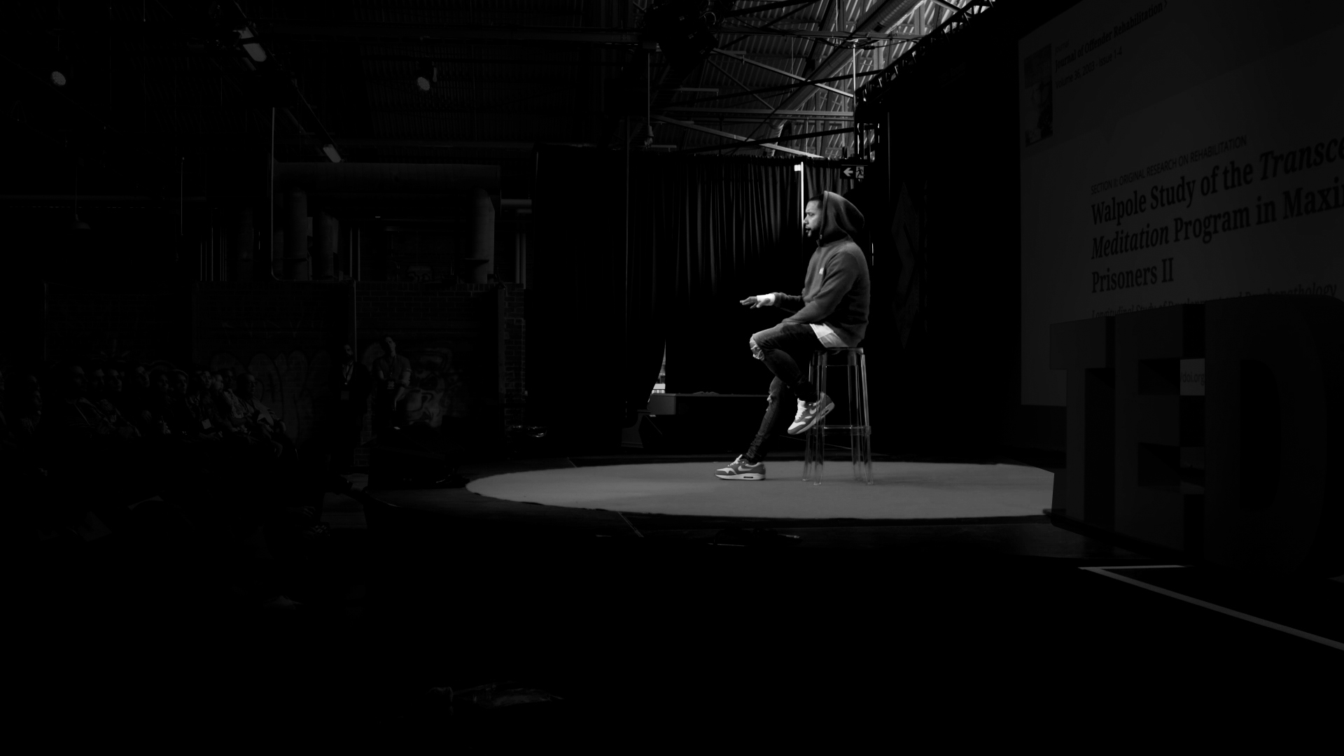 A black and white image of director X onstage at TEDxToronto talking to a crowd